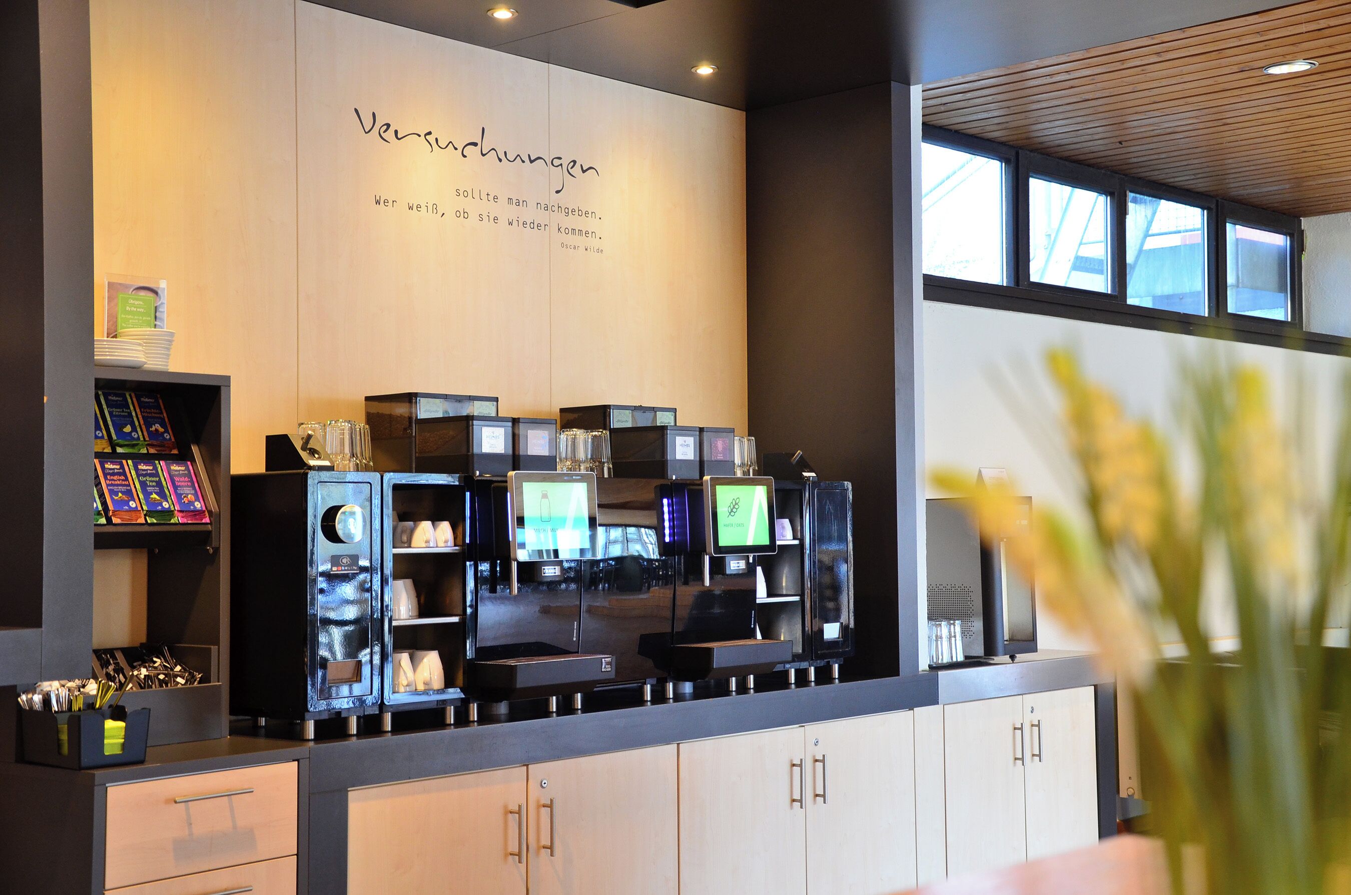 A modern coffee shop with a coffee machine, menu boards, and a wall with text.
