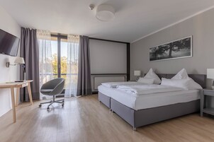 Una habitación de hotel moderna con una cama grande, un escritorio con silla, un televisor y una ventana con cortinas.