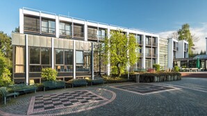 A modern building with large windows and a paved courtyard with benches. - Bildungs- und Tagungshaus Haus Neuland (Bielefeld)