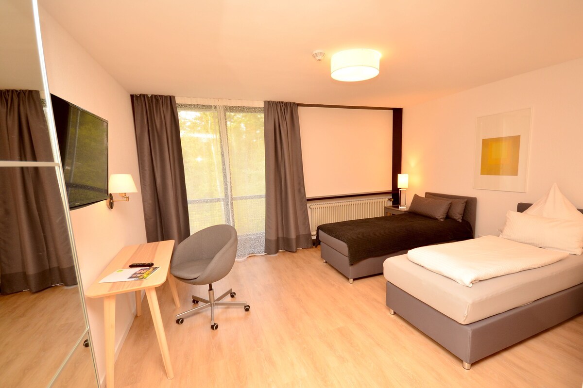 Ein Hotelzimmer mit Bett, Schreibtisch, Stuhl und einem großen Fenster mit Vorhängen.