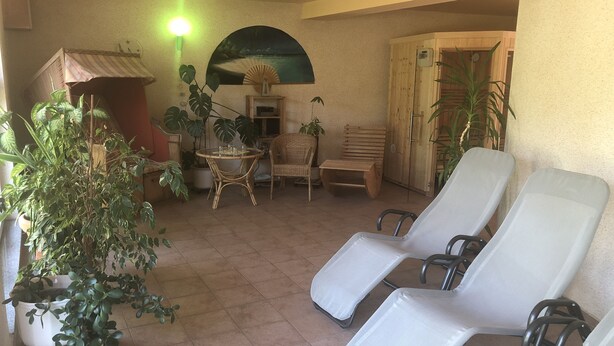 Pátio ensolarado com cadeiras de descanso, uma mesa e plantas em vasos.
