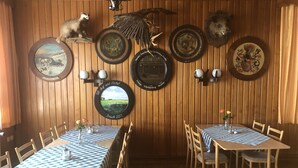Um restaurante com paredes de madeira, toalha quadriculada e diversos quadros e troféus de animais.