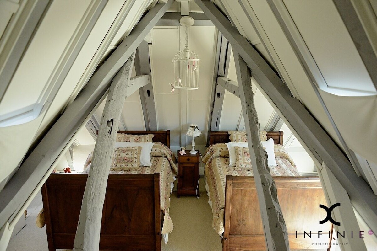 A bedroom with two wooden beds, a hanging light fixture, and a small bedside table with a lamp.