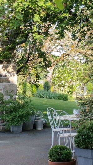 A garden with a white metal chair and table, surrounded by greenery and stone walls. - Domaine du Salabert (Saint-Martial de Gimel)