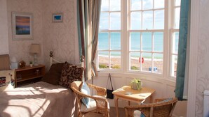 A bedroom with a bed, a chair, a table, and a view of the beach through large windows. - Lyndale Guest House (Weymouth)