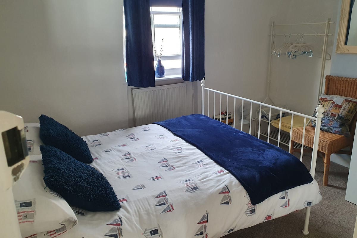A bedroom with a bed, a window with curtains, a chair, and a radiator.