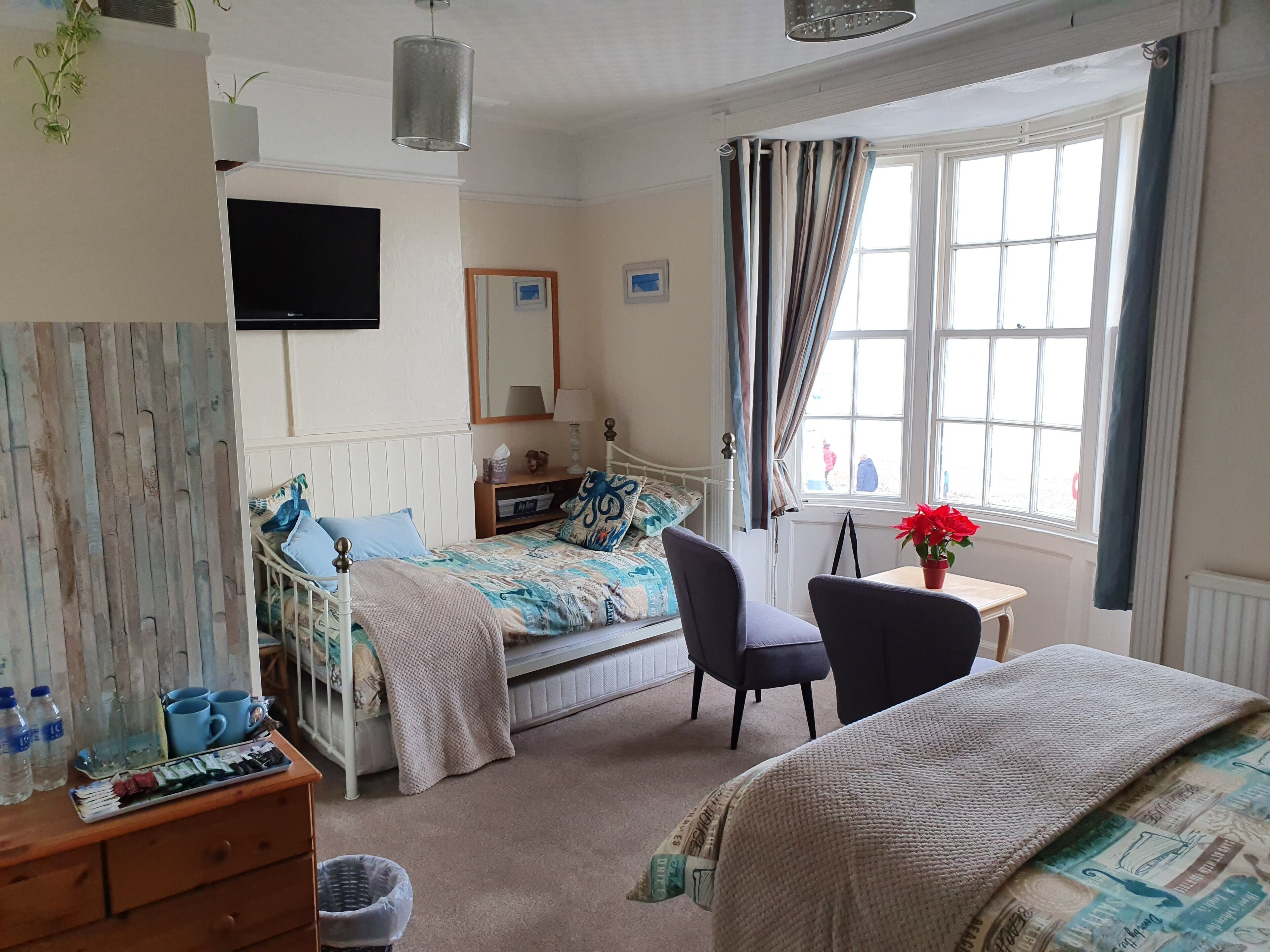 A bedroom with a bed, a desk, a chair, a TV, and a window with curtains.