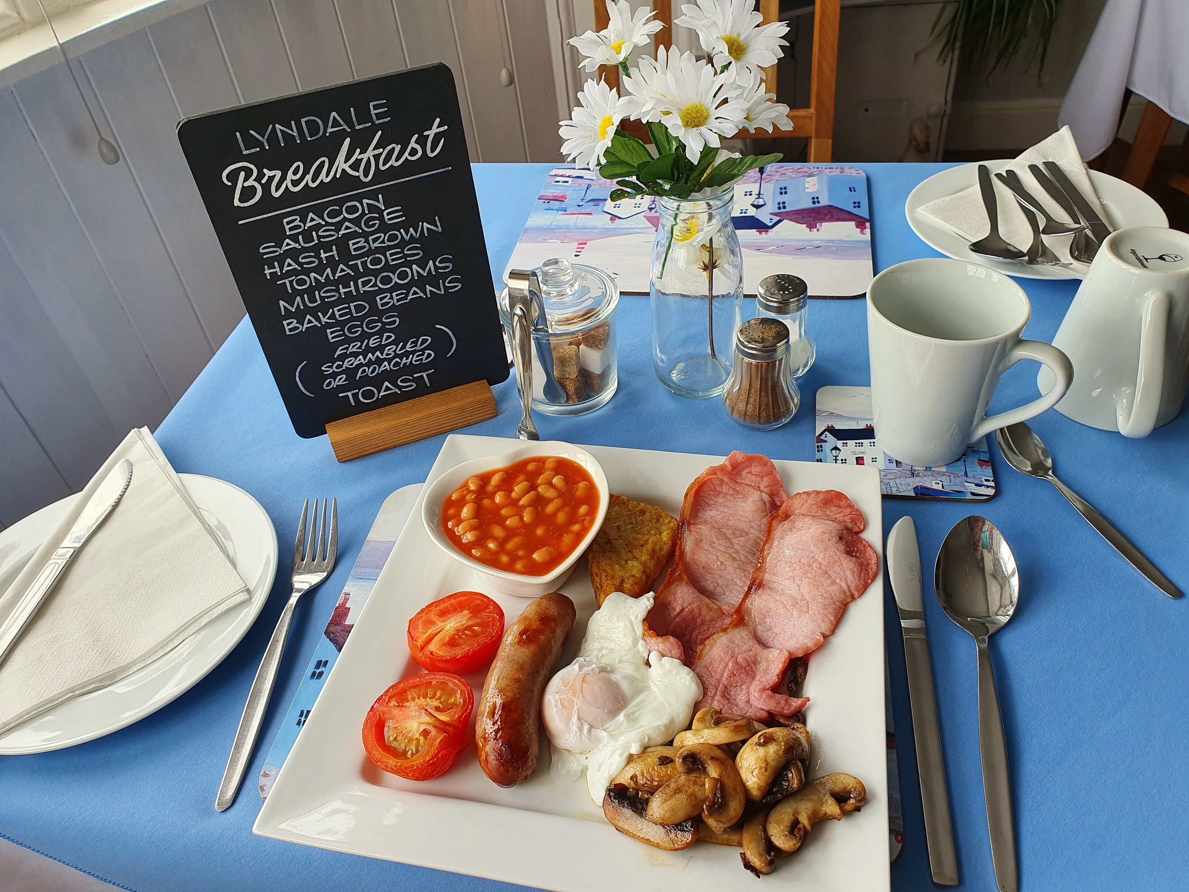 Mesa de café da manhã com um letreiro listando itens como bacon, linguiça e ovos.