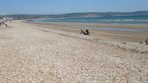 A pebbled beach with a few people and a building in the background. - Lyndale Guest House (Weymouth)