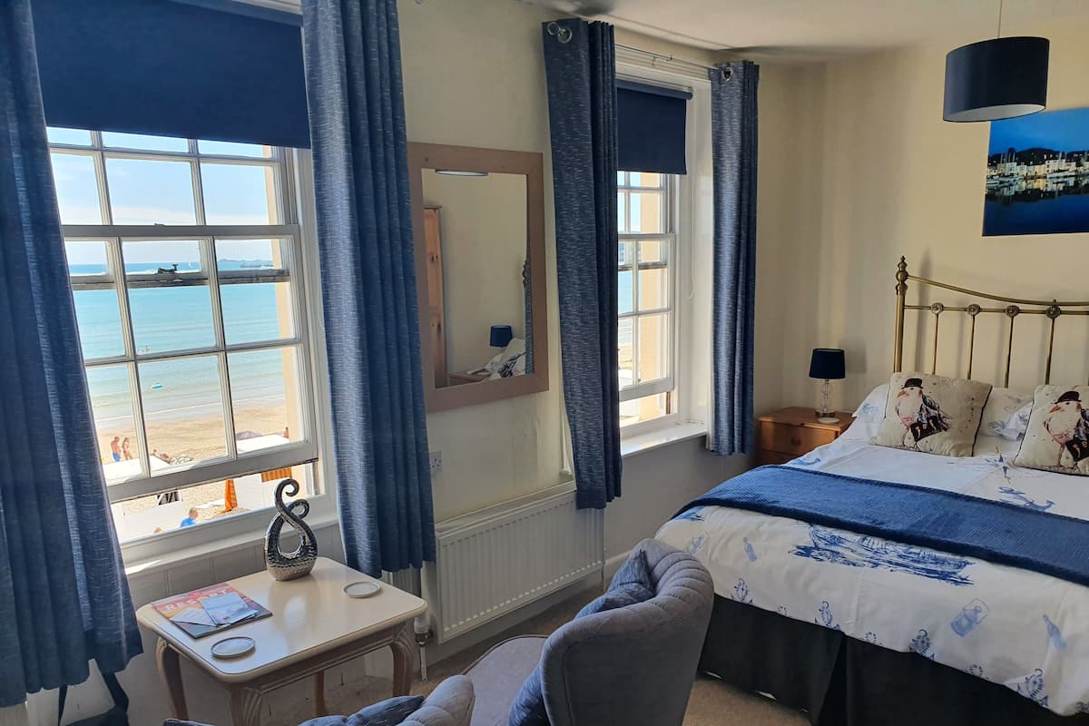 A bedroom with a bed, a chair, a table, and a view of the beach.