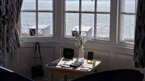 A room with a large window overlooking a body of water, a table with a vase, and two chairs. - Lyndale Guest House (Weymouth)