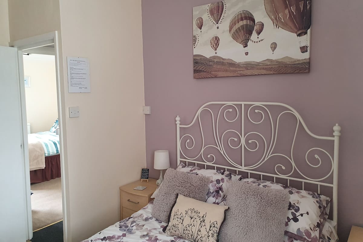 A bedroom with a bed, a nightstand, a lamp, and a painting of hot air balloons.
