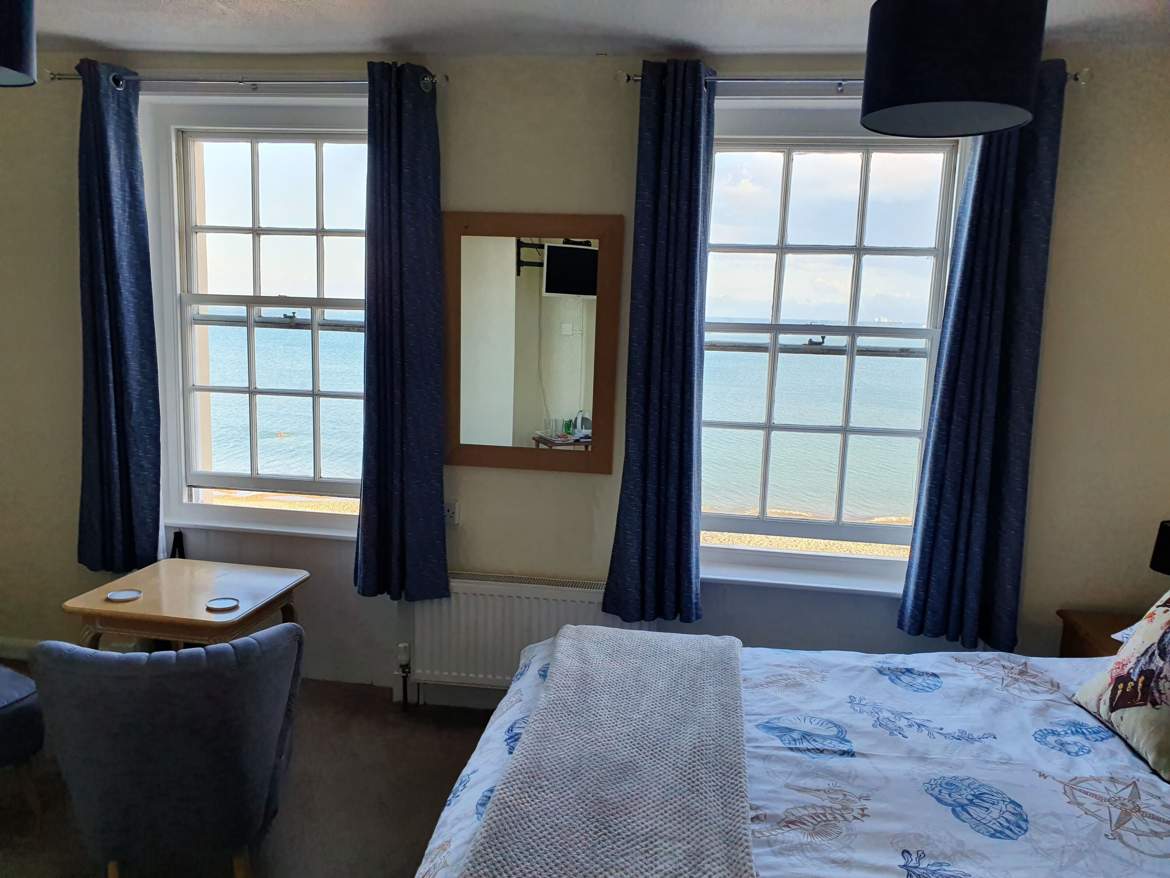 A room with a bed, a small table, a chair, and a window with a view of the sea.