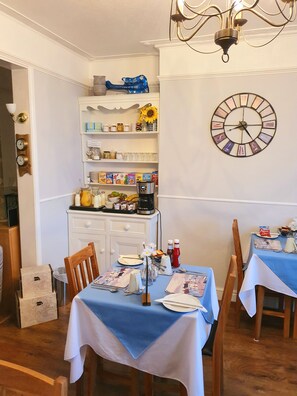 A dining area with a clock, shelves with jars and kitchen items, and a coffee maker on a table. - Lyndale Guest House (Weymouth)