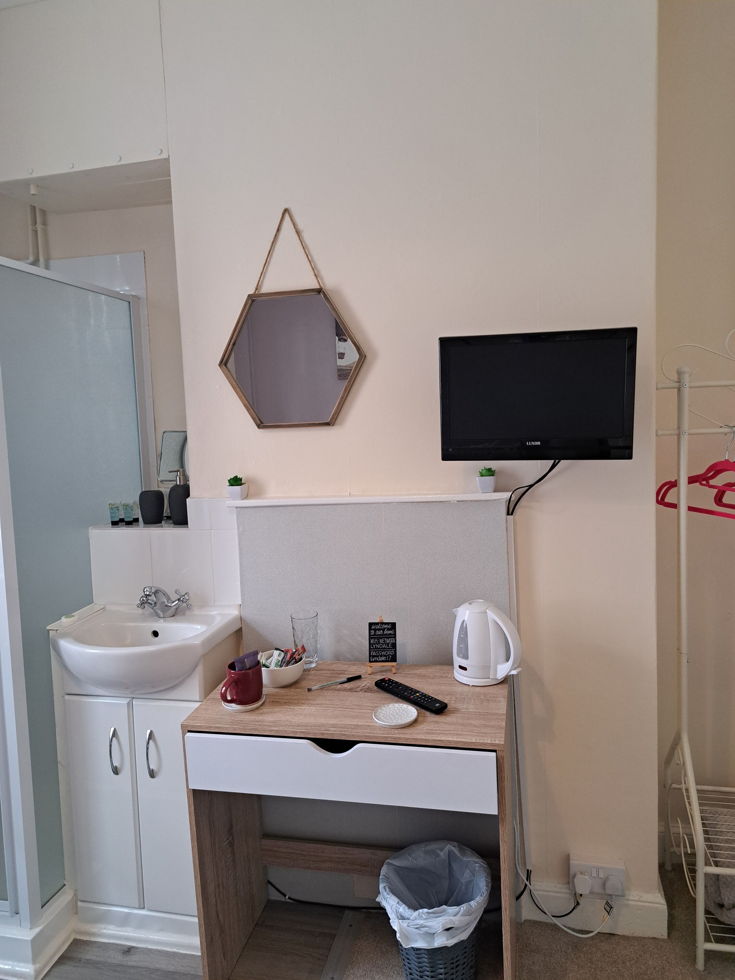 Casa de banho compacta com lavatório, espelho e pequena mesa com chaleira e comando remoto.