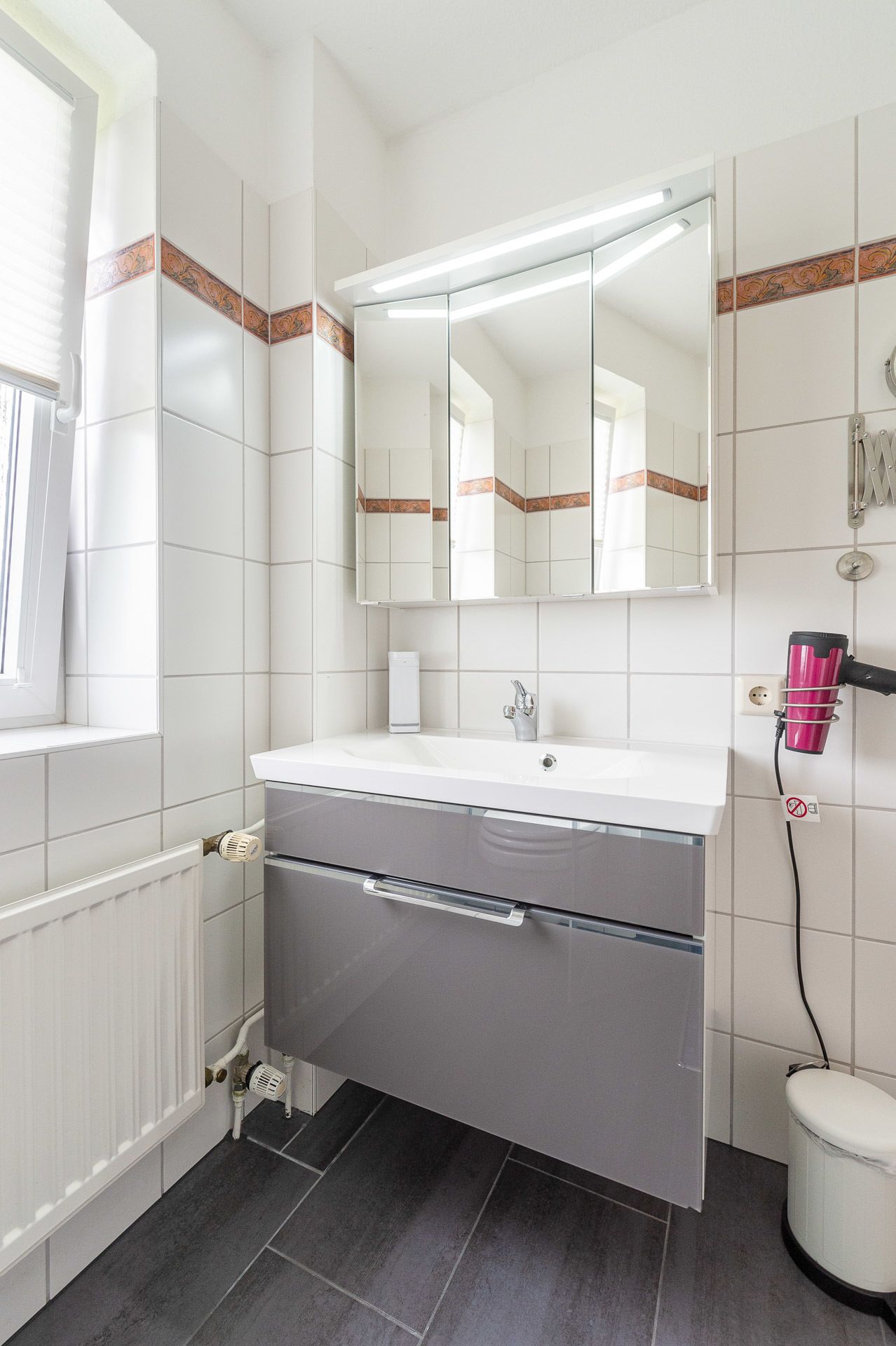A bathroom with a white sink, a mirror, a hairdryer, and a radiator.