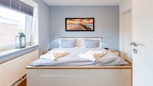 A bedroom with a bed, a nightstand, a window with blinds, a radiator, and a door. - Haus Bendix (Dagebuell)