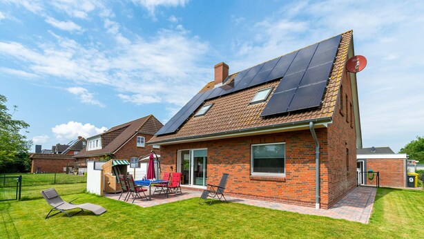 A house with solar panels on the roof, a brick exterior, and a well-maintained lawn with outdoor furniture. - Haus Bendix (Dagebuell)