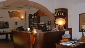 Eine Barbereich mit einer Holztheke, Regalen mit Flaschen, einer Kaffeemaschine und einer Lampe.