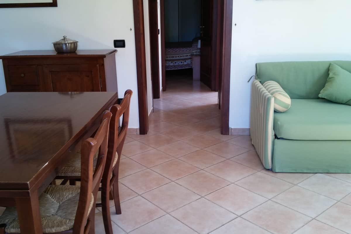 Uma sala de jantar com uma mesa e cadeiras de madeira, um pequeno armário e um sofá verde.