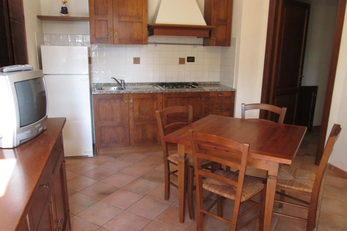 Uma cozinha com armários de madeira, painel de azulejos, fogão a gás e uma mesa de jantar com cadeiras.