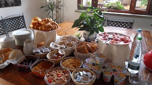 Ein reichhaltiges Frühstücksbuffet mit verschiedenen Speisen, darunter Gebäck, Früchte und Milchprodukte, auf einer Holztischplatte.