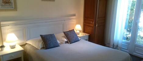 Una cama bien hecha con dos almohadas, una mesita de noche con lámpara y un armario de madera.