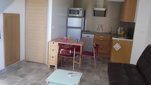 A compact kitchen with a microwave, refrigerator, and a small dining area with a table and chairs. - Sous les Pins de Nages (Nages-et-Solorgues)
