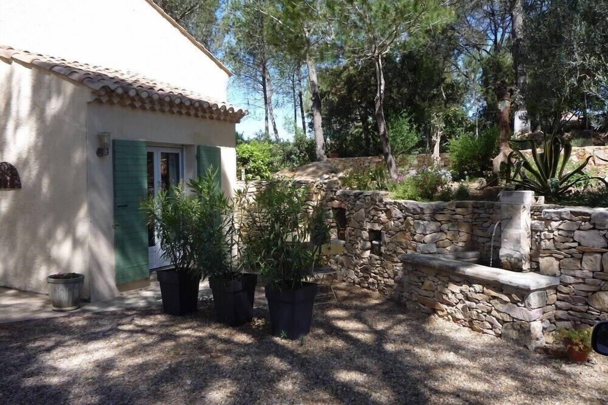 Une maison rustique avec un mur en pierre, un petit jardin agrémenté de plantes en pot et une porte en bois.