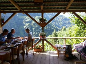 A wooden deck with a table and chairs, a sofa, and a view of a forested mountain range.