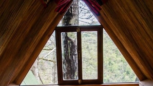 A cozy, triangular wooden room with a bed, a window, and a view of trees.