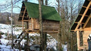 A wooden birdhouse with a green roof, situated in a forested area with snow on the ground.