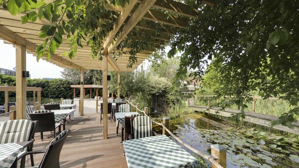 Un patio al aire libre con mesas y sillas de madera, una terraza de madera y un estanque con nenúfares.