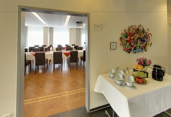 Un salón de conferencias con mesas y sillas, un cartel de reunión y una mesa con alimentos para el desayuno.