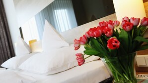 Habitación de hotel con cama, almohadas blancas, un jarrón de tulipanes rojos y un ventanal con cortinas.