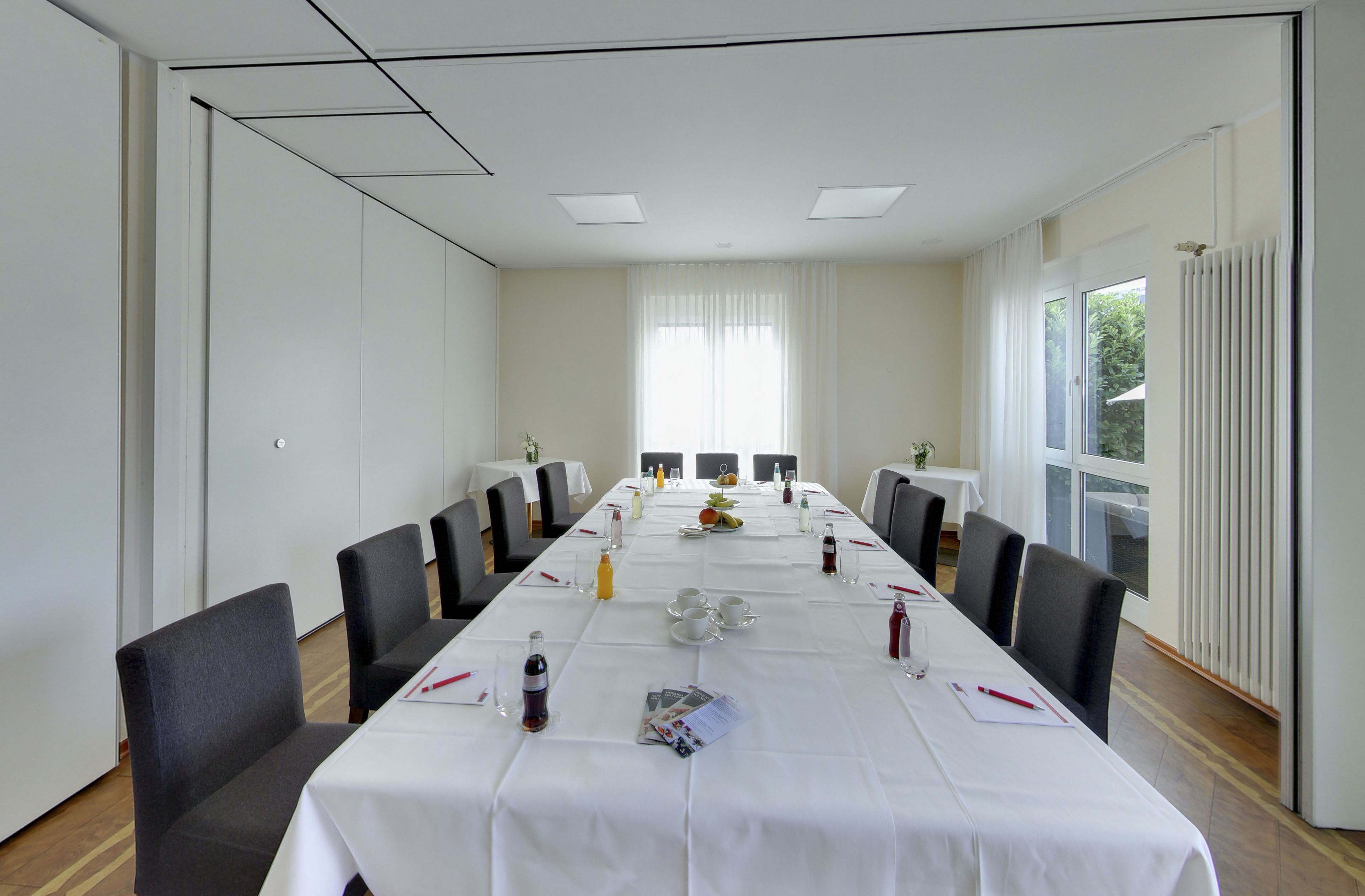 Un salón de conferencias con una larga mesa, sillas y un ventanal con cortinas.