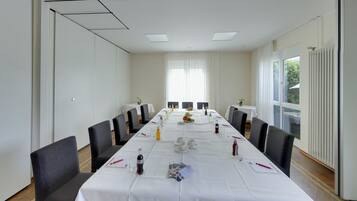 Un salón de conferencias con una larga mesa, sillas y un ventanal con cortinas.