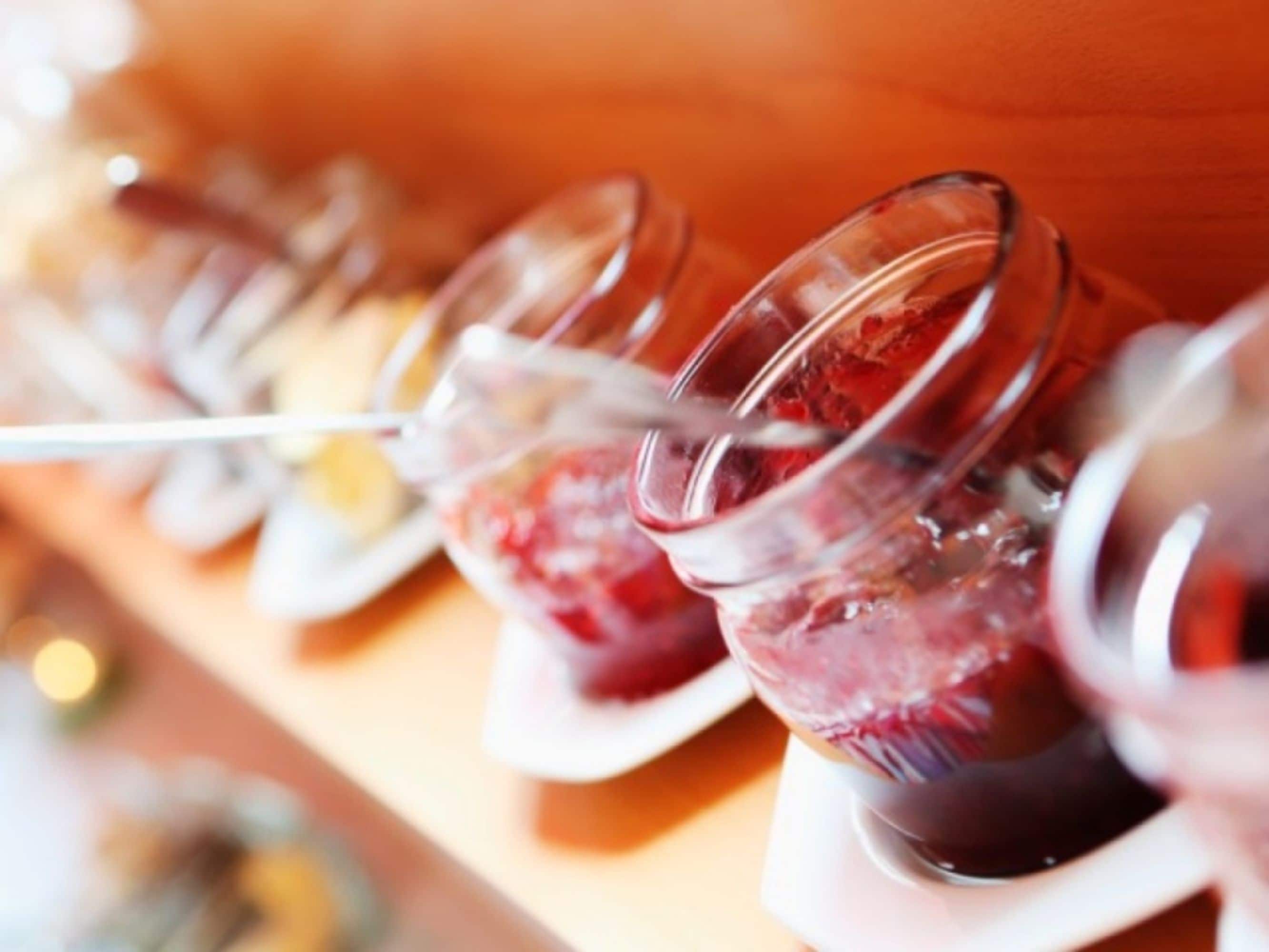 Una hilera de vasos transparentes llenos de una bebida roja, probablemente un ponche de frutas o jugo, sobre una superficie de madera.