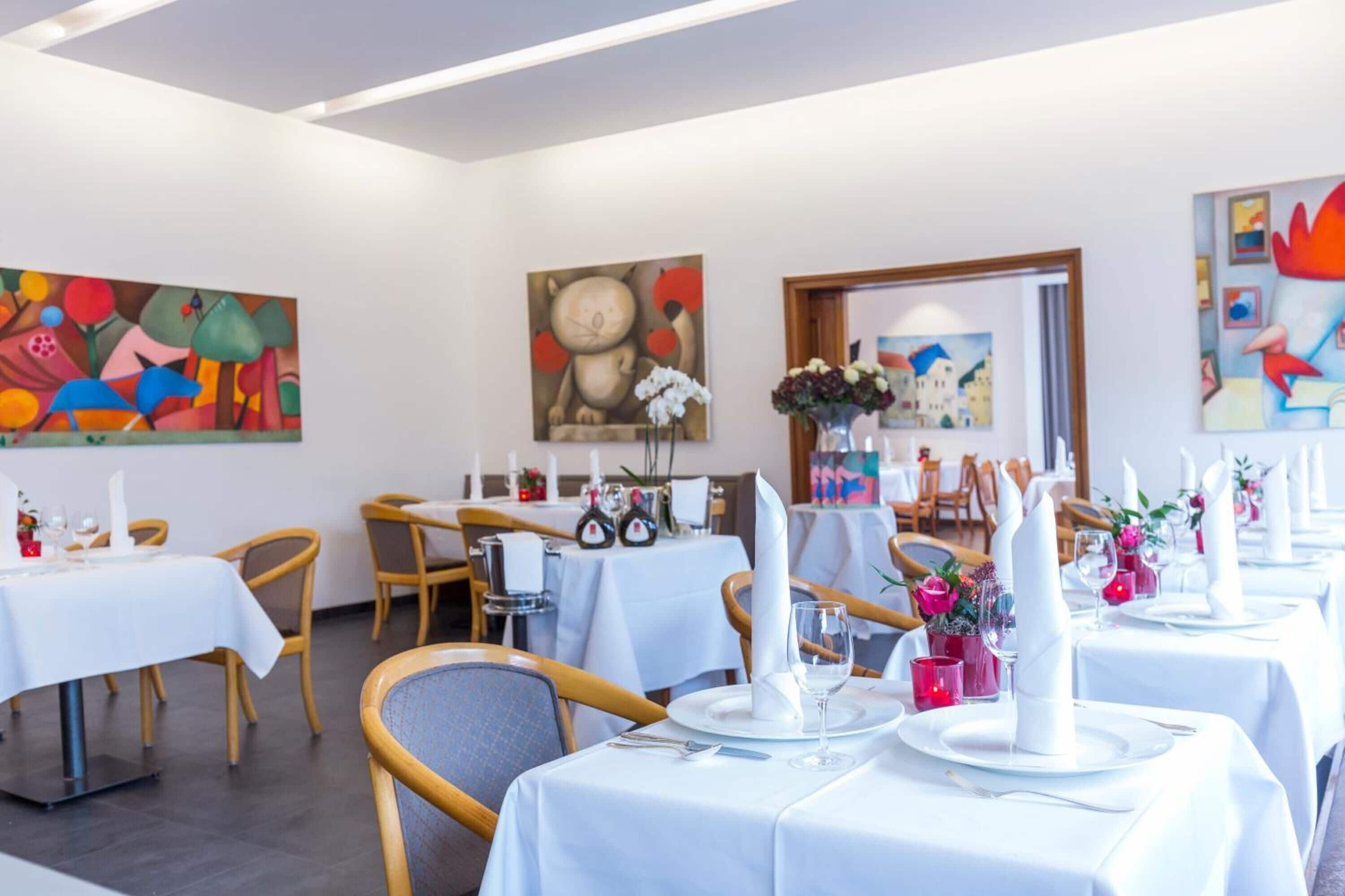 A restaurant with white tablecloths, wooden chairs, and artwork on the walls.