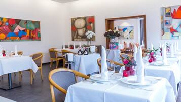 A restaurant with white tablecloths, wooden chairs, and artwork on the walls.