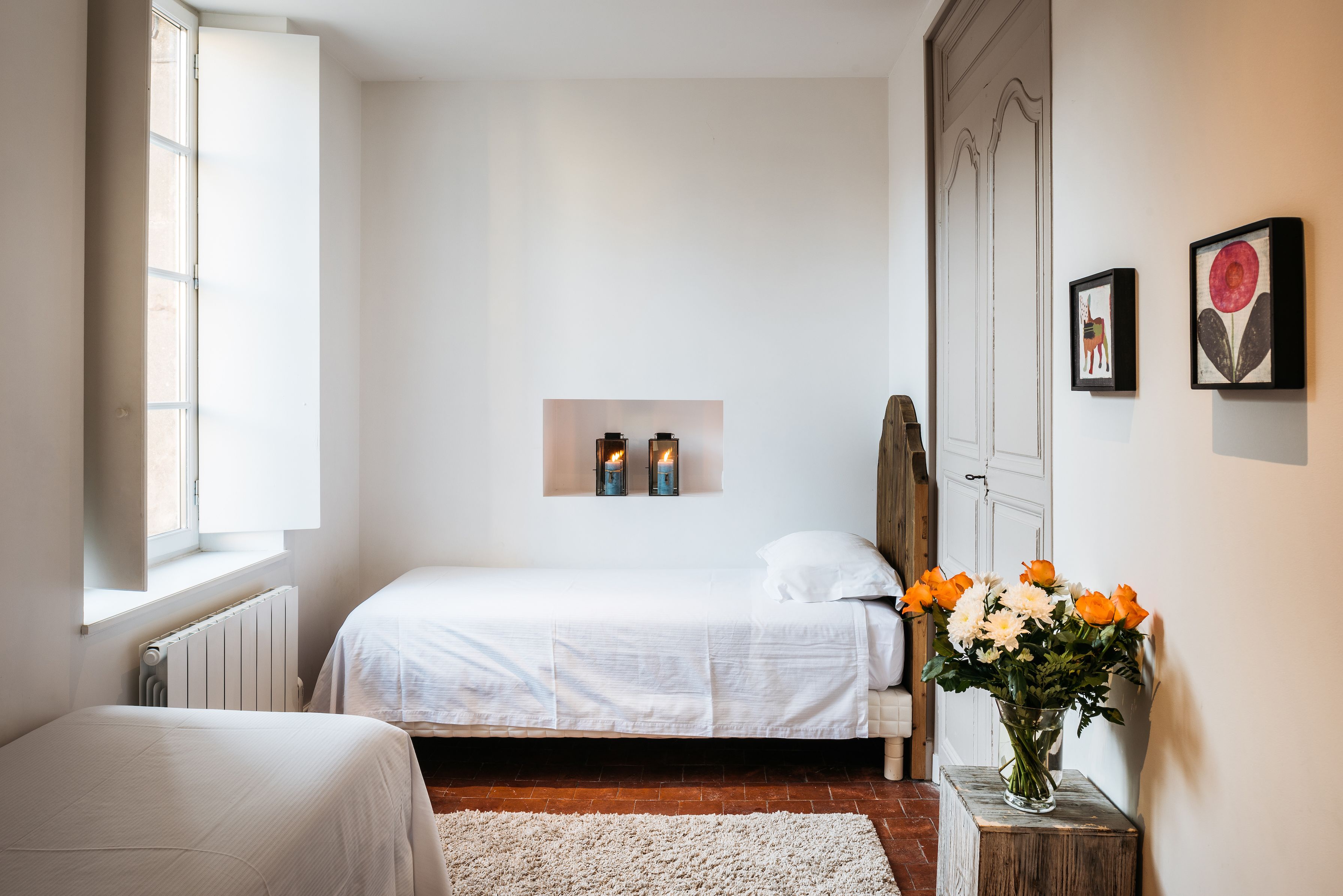 A bedroom with a bed, a nightstand, a vase of flowers, and a framed picture on the wall.