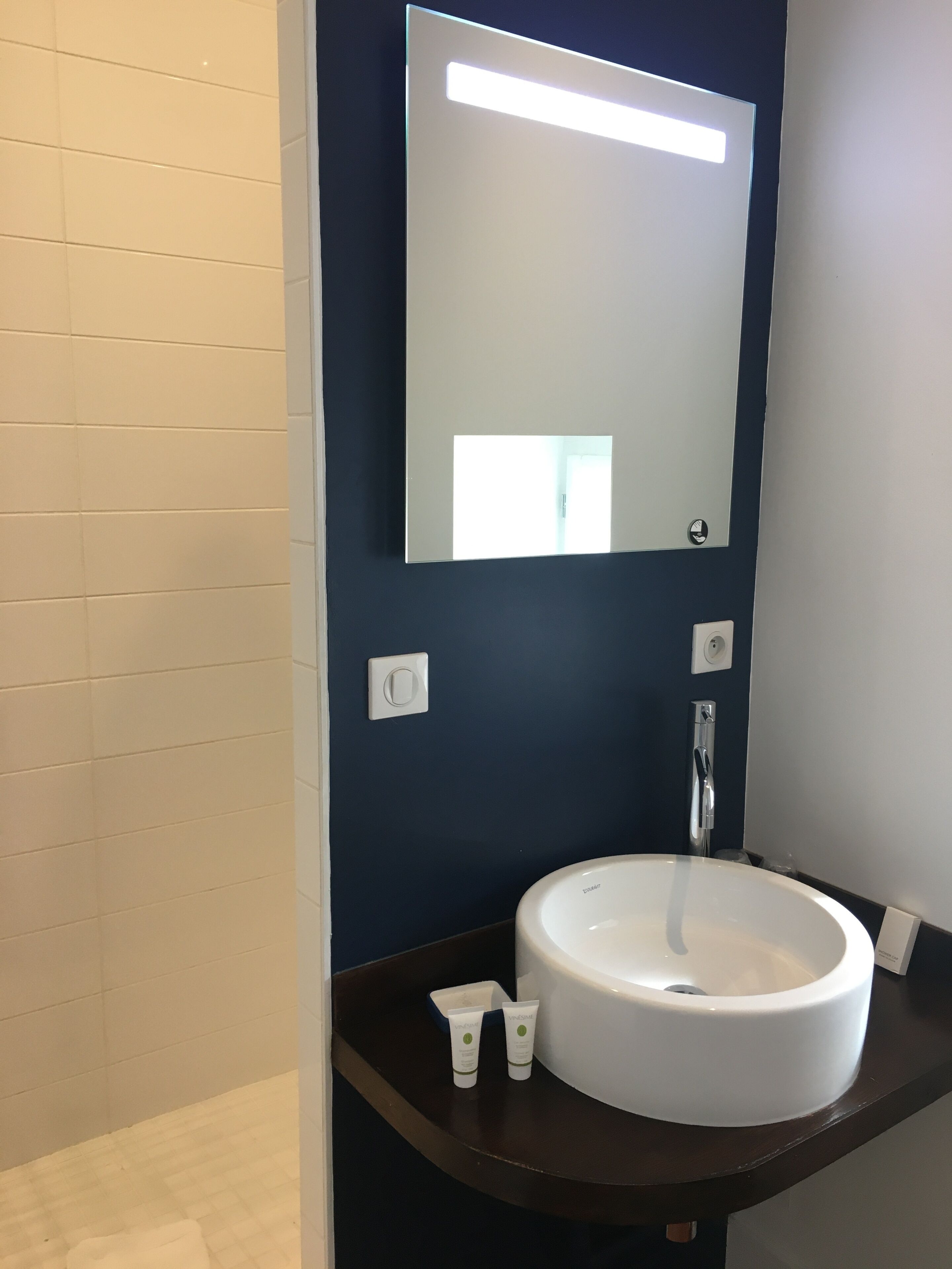 A bathroom with a white sink, a mirror, and a dark blue wall.