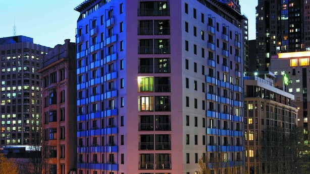A multi-story hotel with a prominent 'Hyland' sign, surrounded by other buildings and a busy street at night. - Sydney Suites (Sydney)