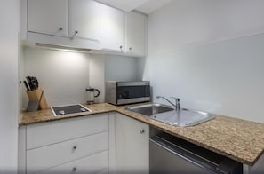 Una cocina compacta con armarios blancos, encimera de granito, microondas integrado y pileta de acero inoxidable.