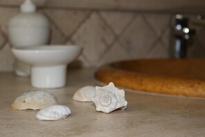 A kitchen counter with a sink, a white bowl, and three seashells.