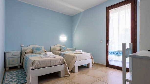 A bedroom with two beds, a nightstand, a dresser, and a window with a view. - B&B Sardinia For You (Oristano)