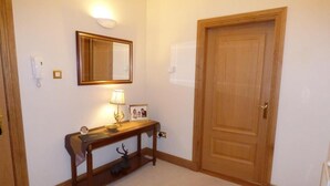 Un pasillo con una puerta de madera, una consola con una lámpara, un espejo y una fotografía enmarcada.