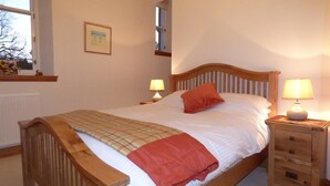 Un dormitorio con una cama de madera, dos mesitas de noche con lámparas, una ventana con vistas y un radiador.