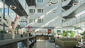 Un moderno vestíbulo de hotel con una zona de bar central, áreas de descanso y una escalera que sube a los pisos superiores.