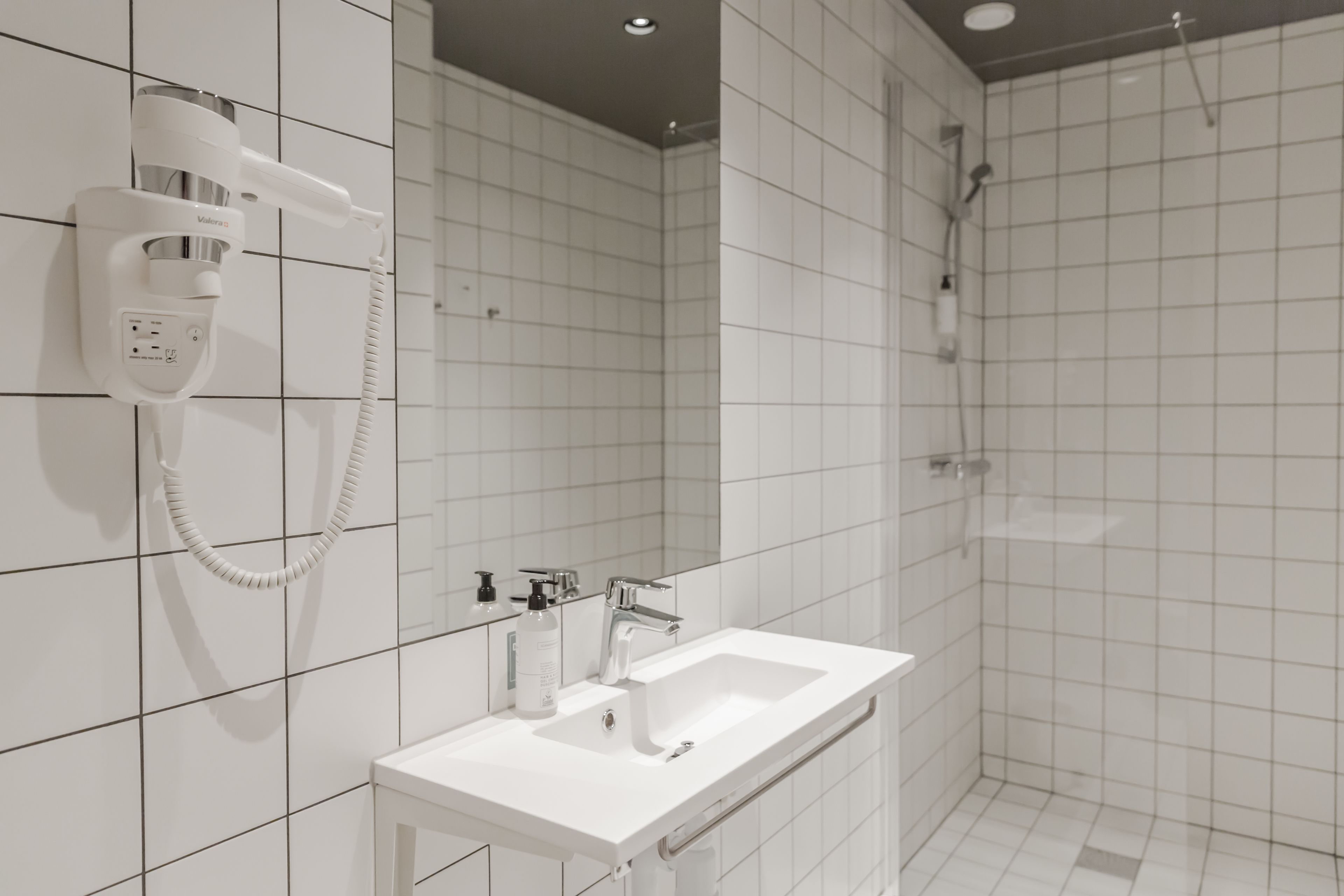 Ein modernes Badezimmer mit einem weißen Waschbecken, einem Spiegel und einem an der Wand befestigten Föhn.